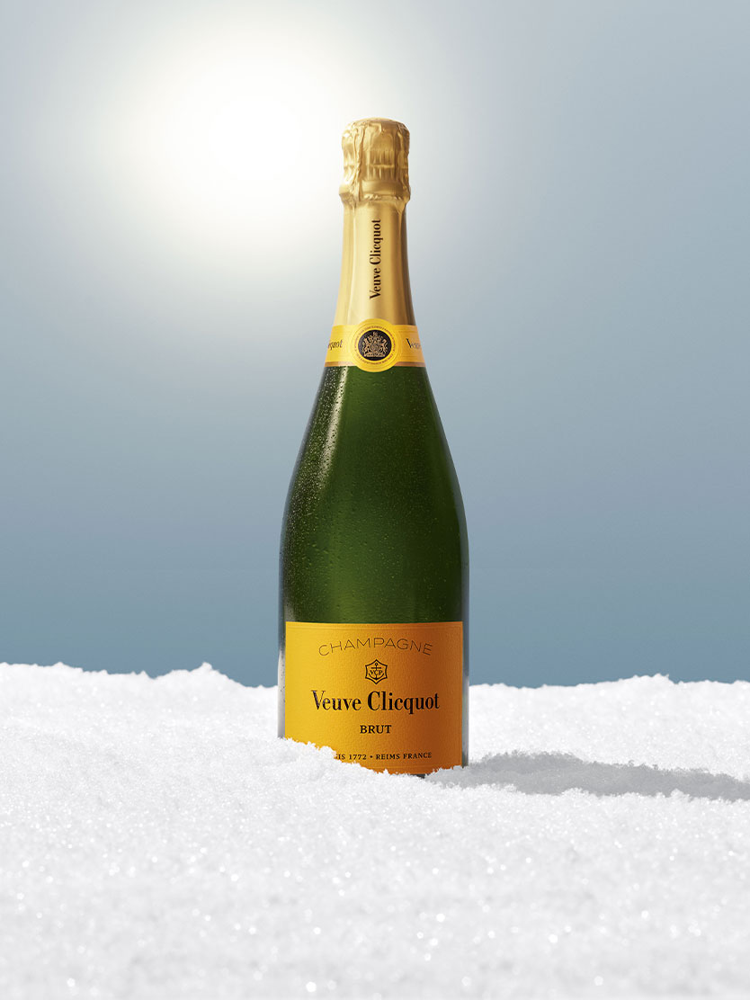 Veuve Clicquot champagne bottle upright in snow with sunlight in the background.
