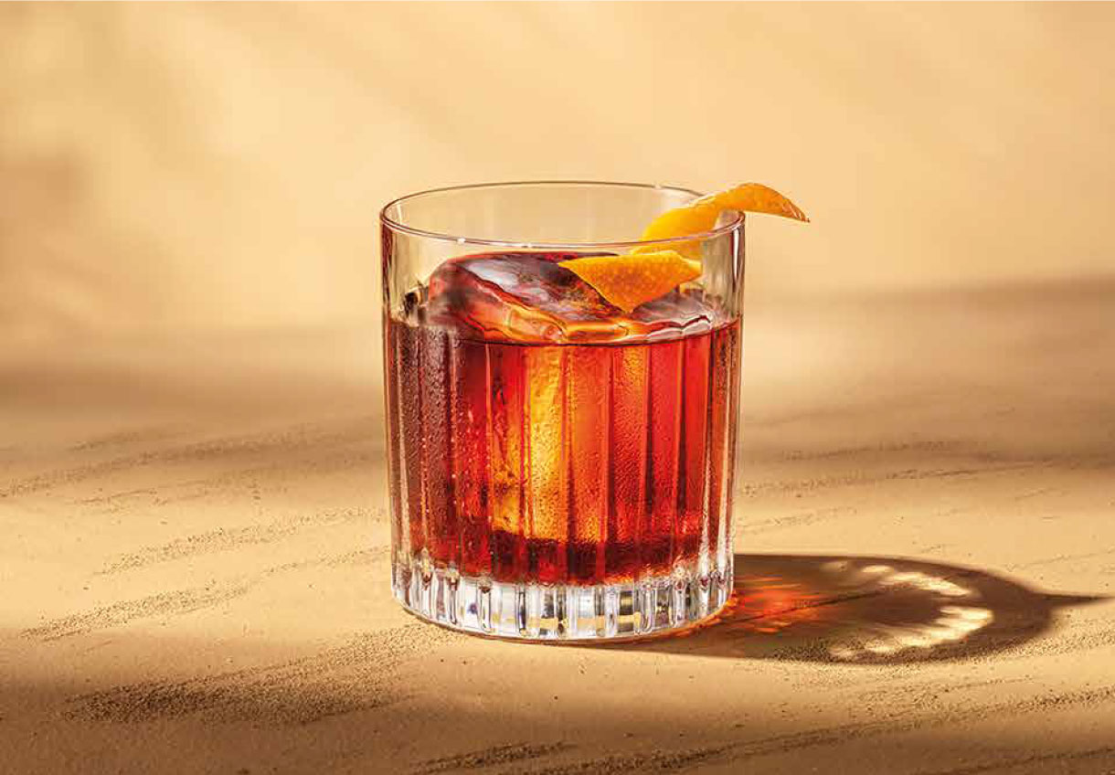 Red cocktail with ice and orange peel garnish.