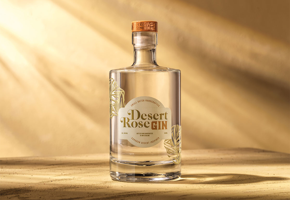 A clear bottle of Desert Rose Gin with a wooden cap, set against a warm, sunlit background.