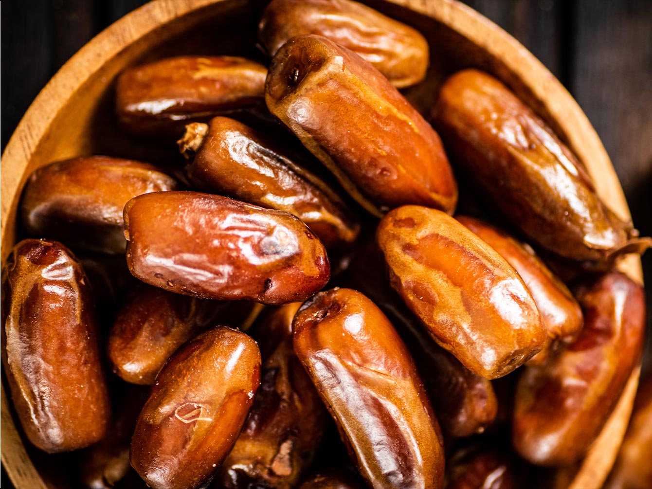 Wooden bowl filled with glossy brown dates.